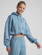woman wearing a light blue hoodie and matching pants on a plain background.